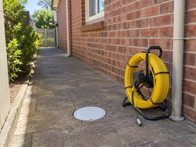Capped drain inspection opening on a brick house side path with a camera reel beside it in Thornleigh