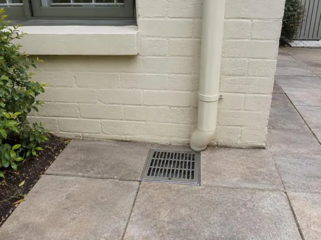 Outdoor gully grate beside painted brick wall with dry paving in Pennant Hills